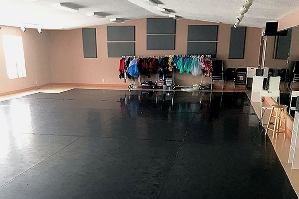 A dance studio with natural light coming in through windows on the left. A rack of costumes along the far wall.