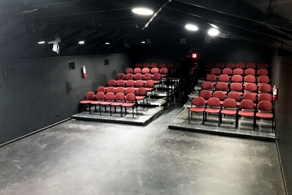 Black box theatre with several rows of red chairs on risers with a row down the middle