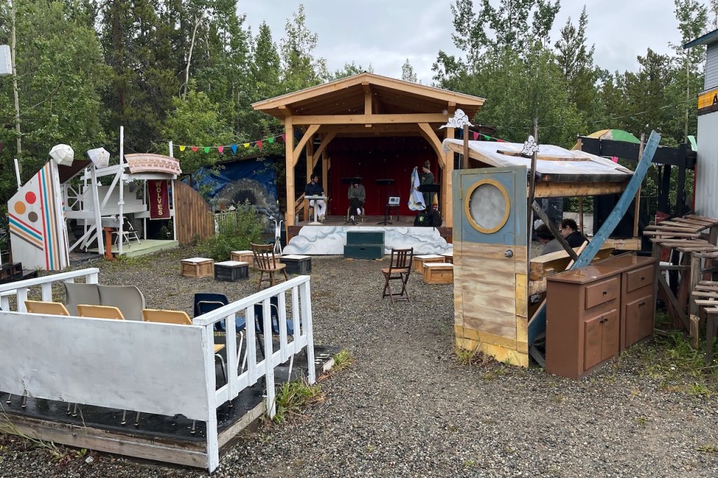 A covered outdoor stage with a collection of old set pieces placed in a seating arc