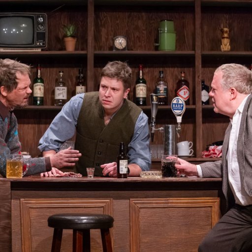 Two men at a bar in discussion with the bartender