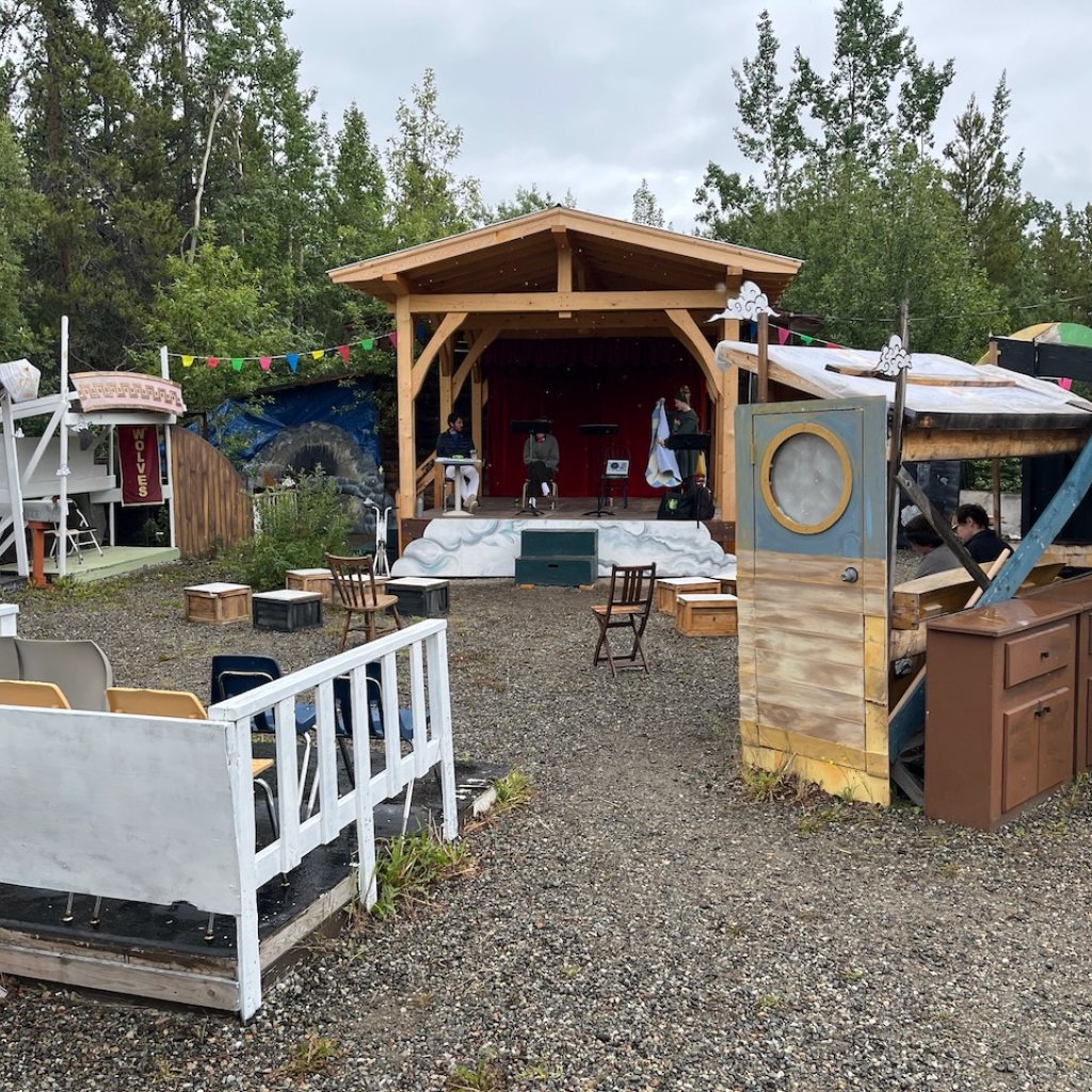 A covered outdoor stage with a collection of old set pieces placed in a seating arc