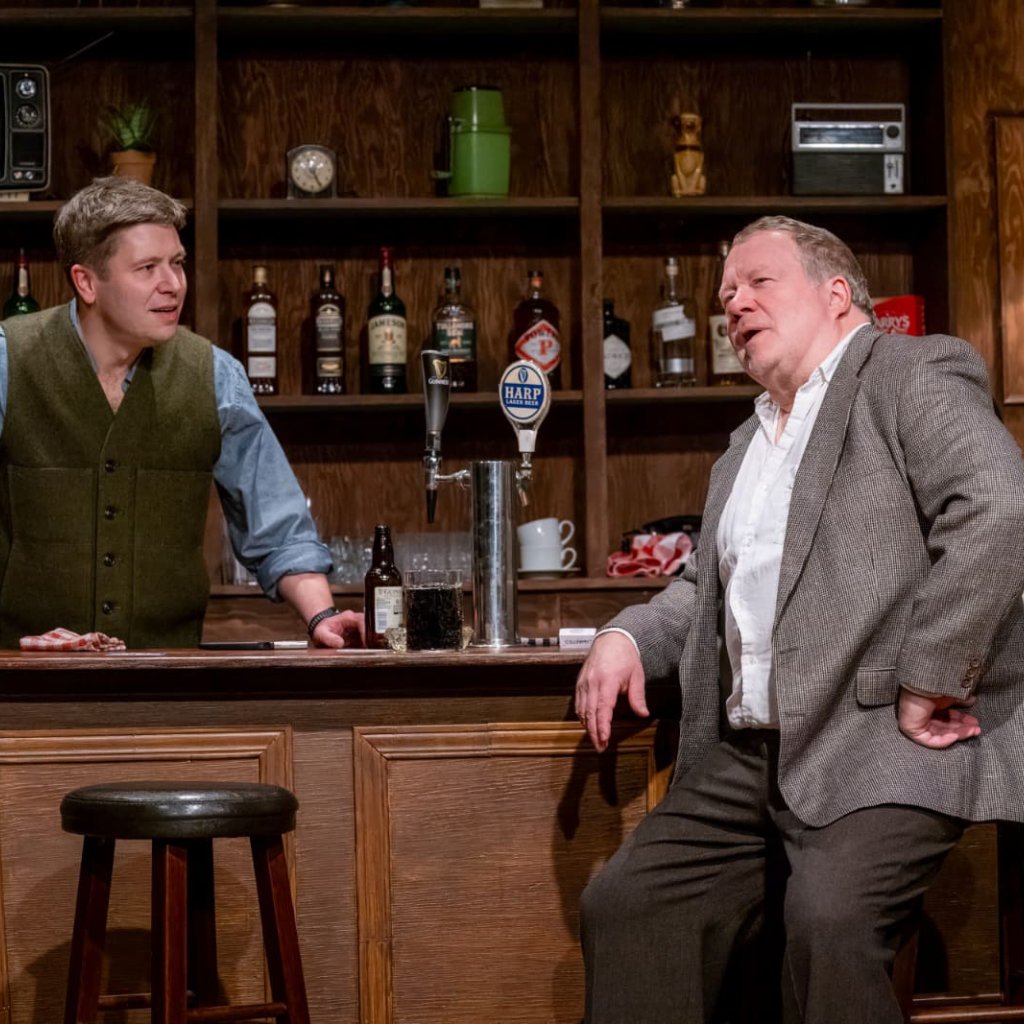 A man sitting at a bar stool, talking to the bartender