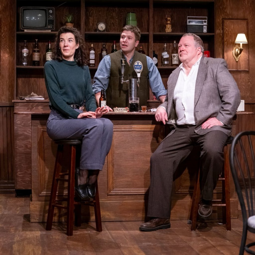A man and woman sitting at barstools with a bartender looking on behind them