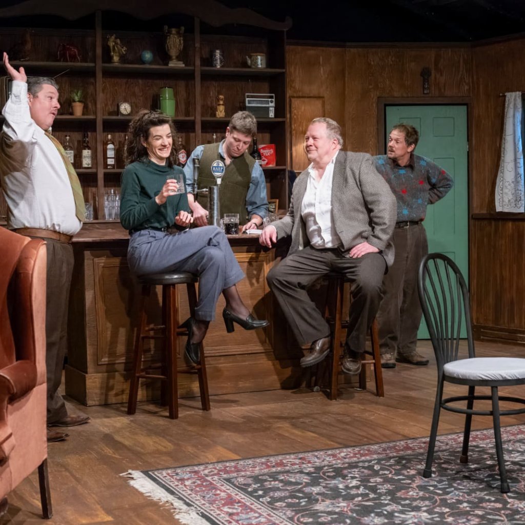 A group of people in an Irish pub. The man on the left side has his arm raised