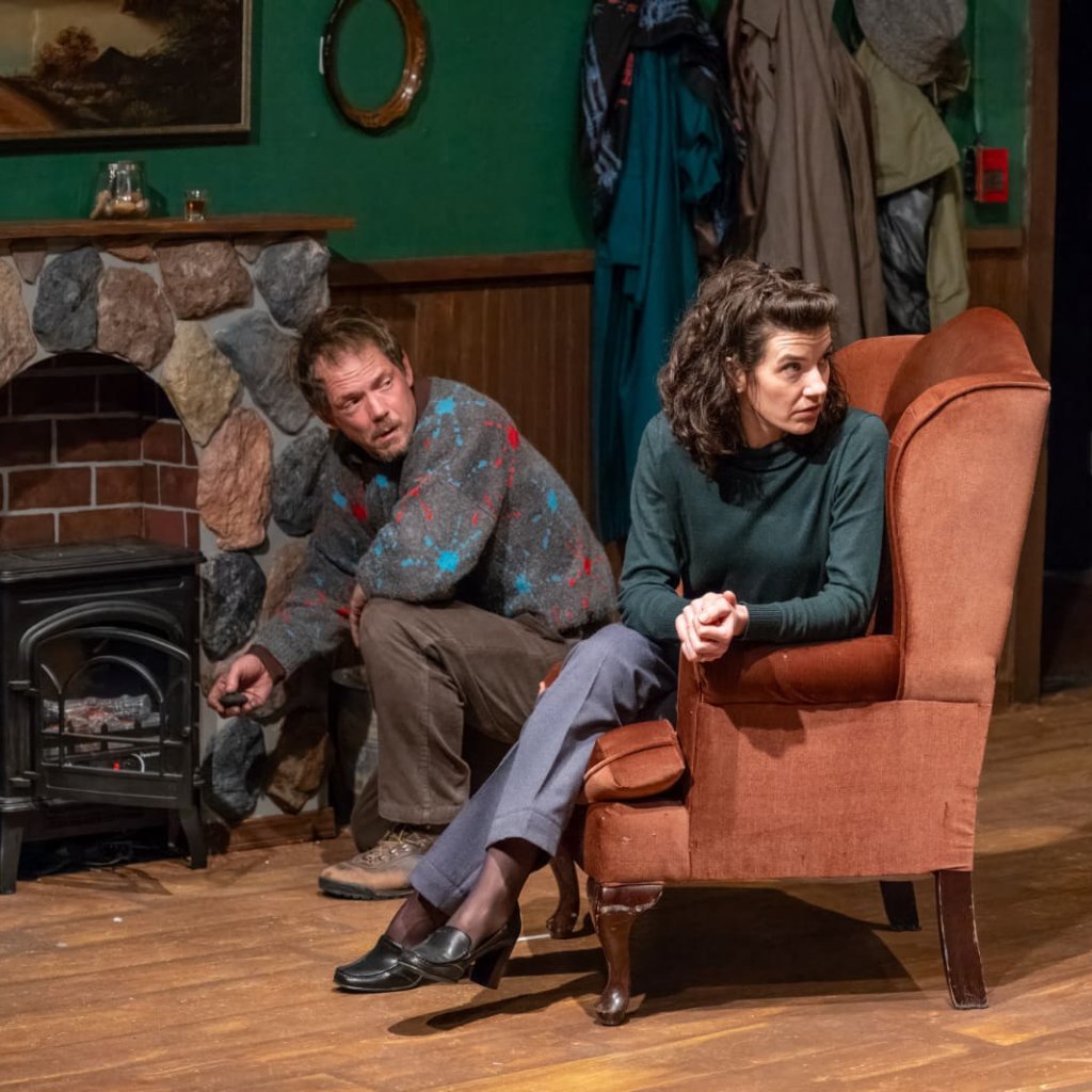 A woman sitting in an armchair in front of a man crouching to stoke a fire