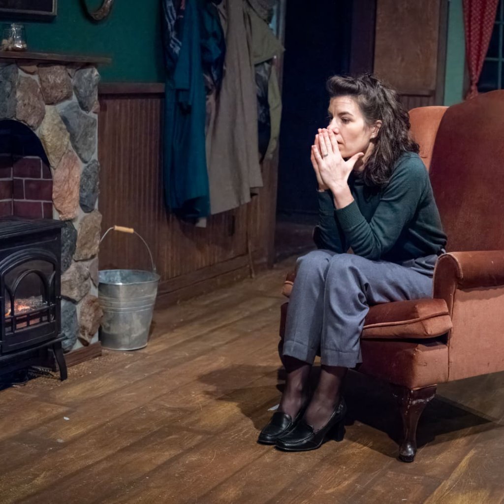 A woman sitting in a red armchair next to a fireplace holds her hands up to her face
