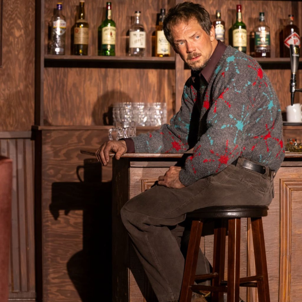 A man sitting on a bar stool looks back over his shoulder