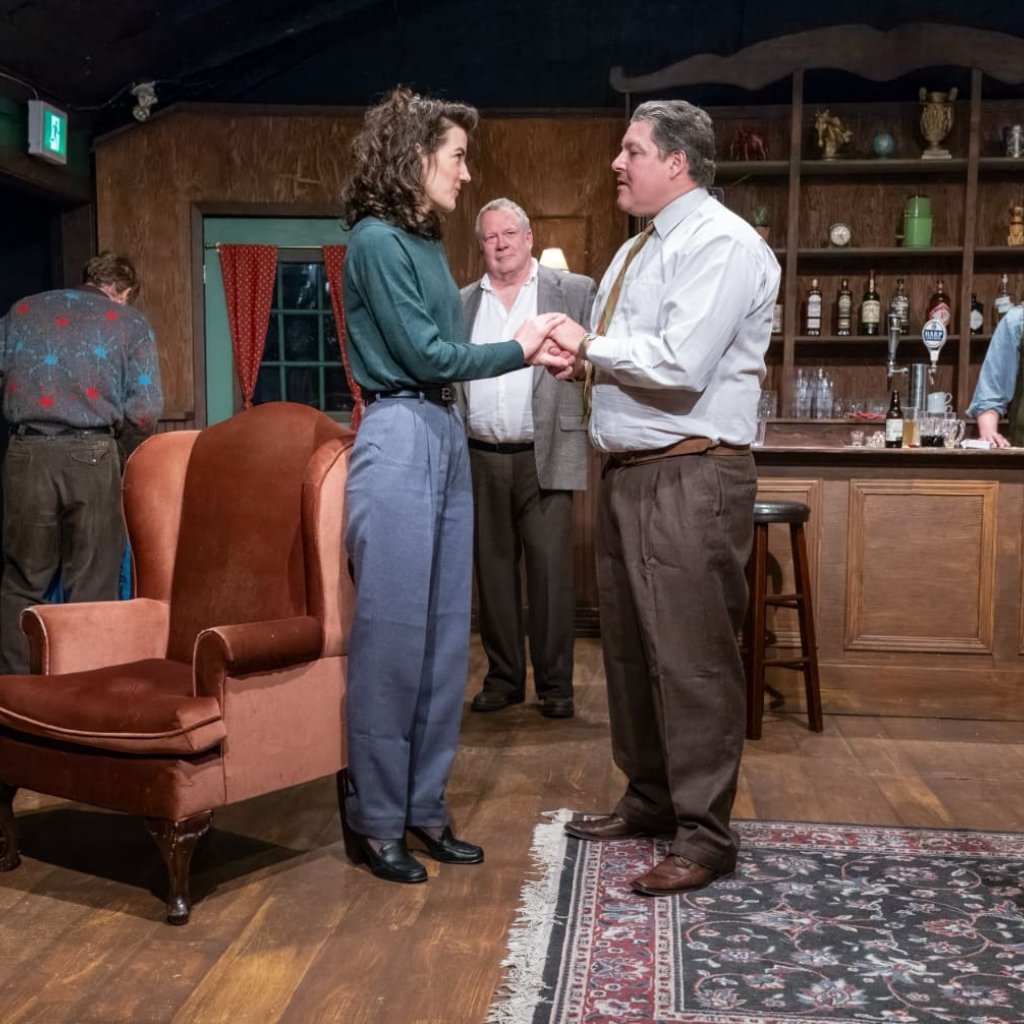 A man and woman hold hands and speak in the middle of an Irish pub