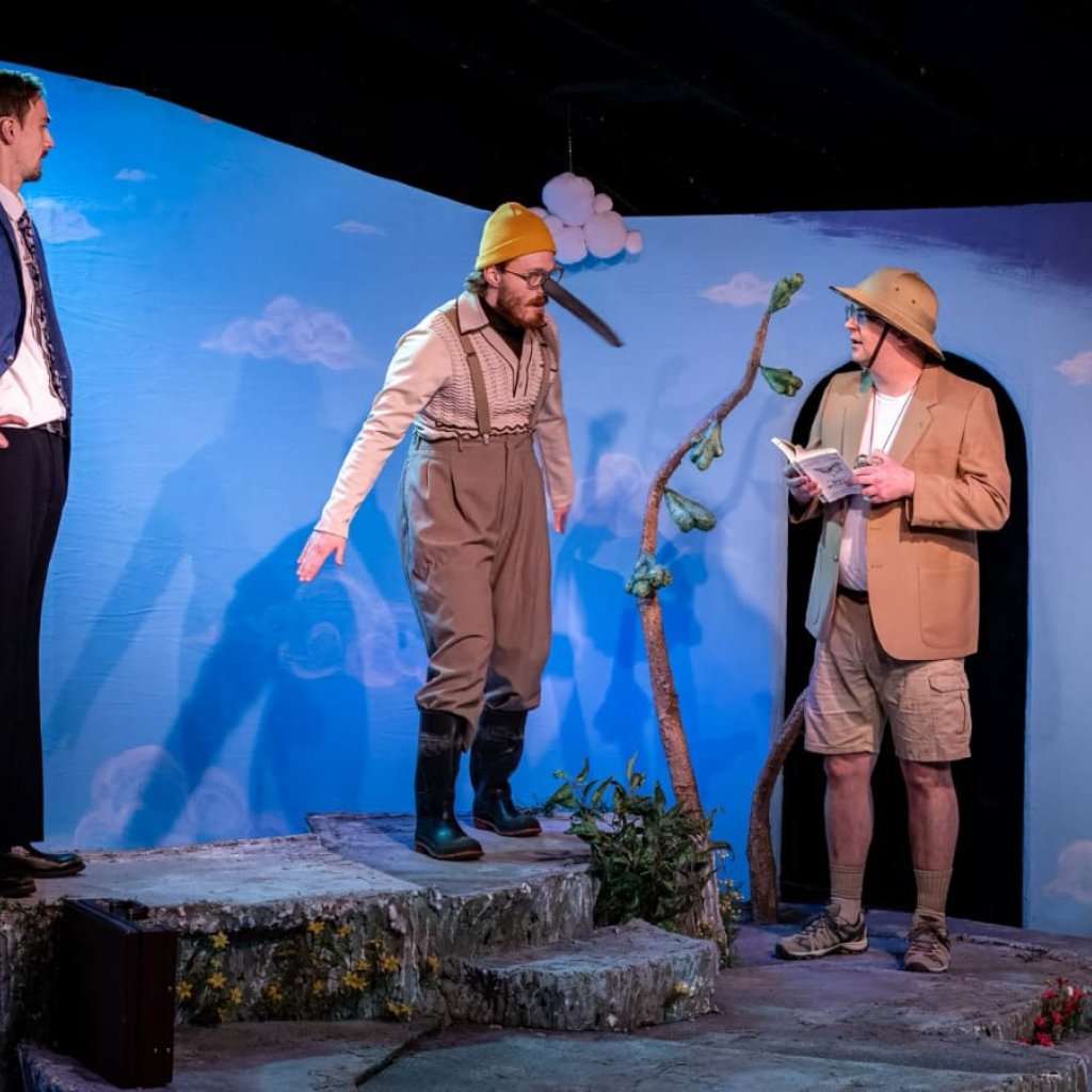 A man with a long black beak and yellow toque stands with arms spread between two men