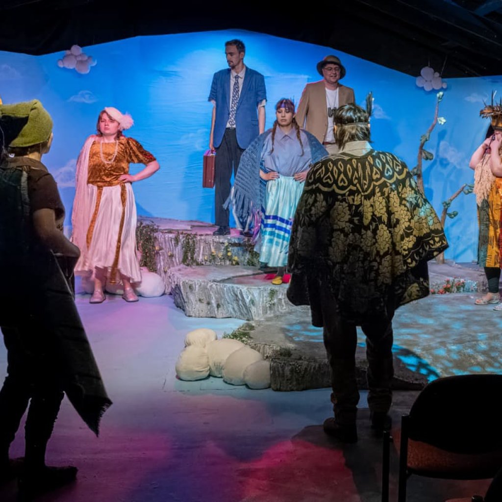 A group of people in bird costumes stand in a circle in front of two men