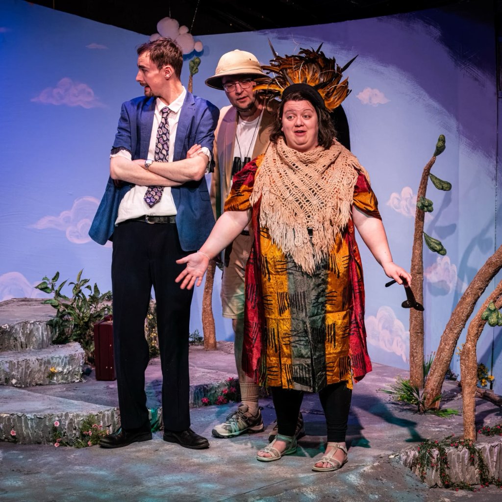 A woman with a hat made of feathers speaks while two men look on