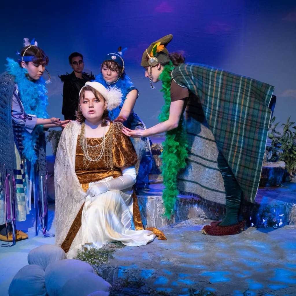 A person dressed as a nightingale is seated and surrounded by three other bird characters leaning toward them