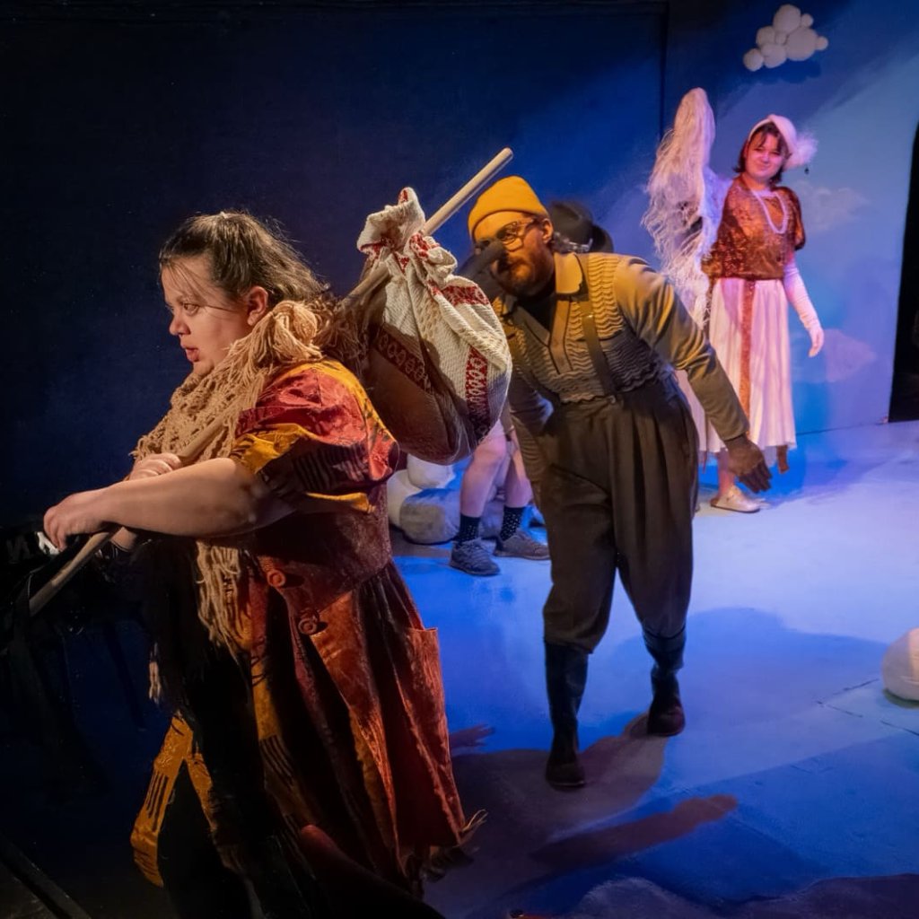 A woman walks away with a bindle over her shoulder while a man dressed as a sandpiper watches her go